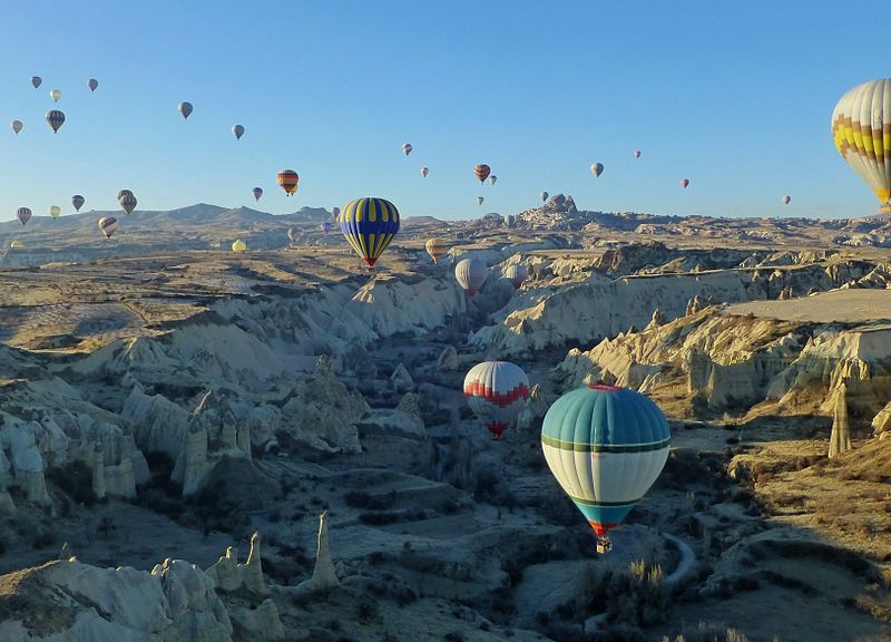 Hot air balloons hover over a scenic valley in Cappadocia, Turkey